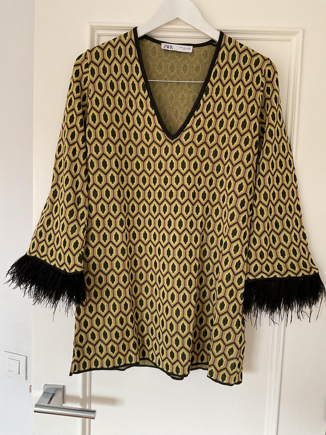 Blouse hanging on a hanger, with yellow and black geometric print, black fringed sleeves. Visible label: ZARA.