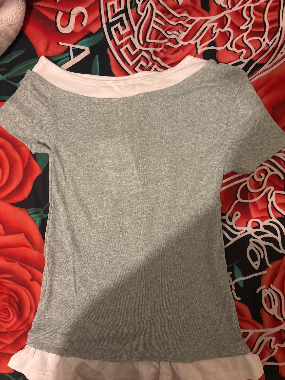 Grey short-sleeved T-shirt on a bedspread with a red rose design and black and white geometric patterns.