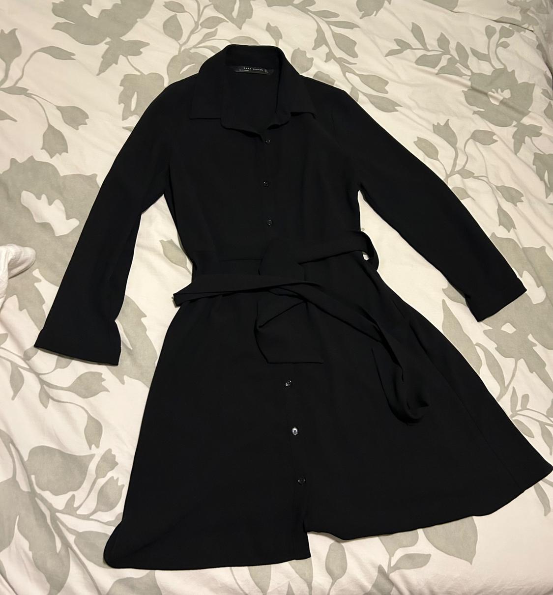 Long-sleeved black dress with a belt and front buttons, on a bed with a grey and white leaf-patterned quilt.