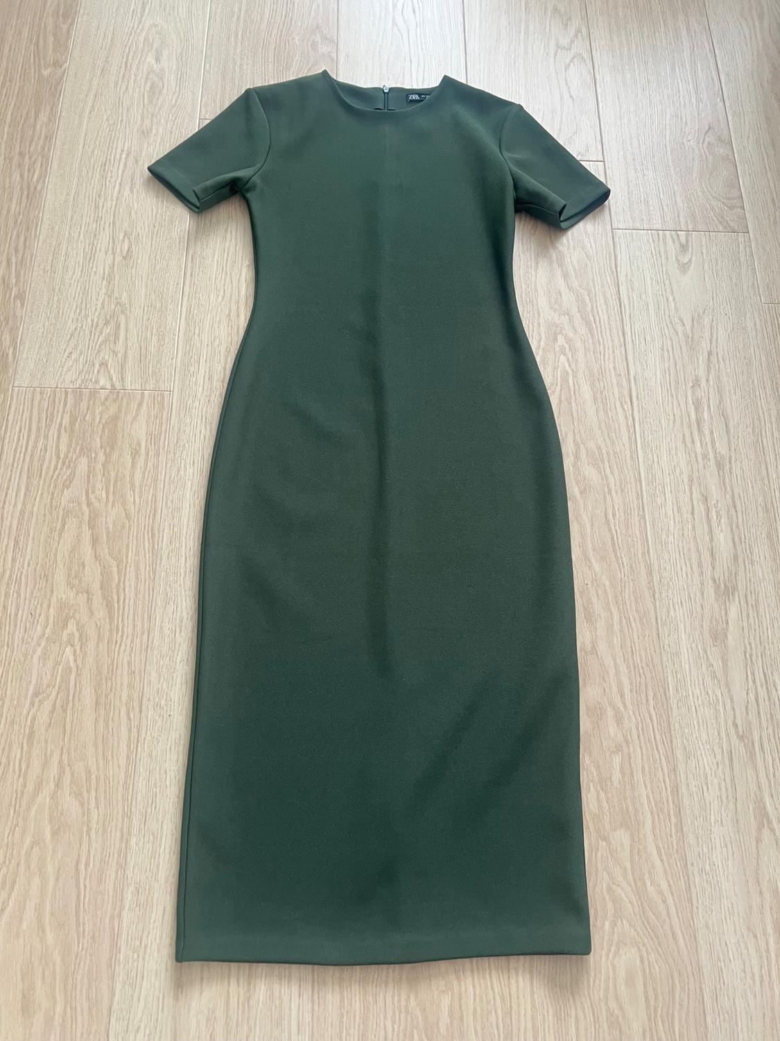 Dark green, short-sleeved, round-neck dress with a fitted silhouette, laid out on a light wood floor. ZARA label.