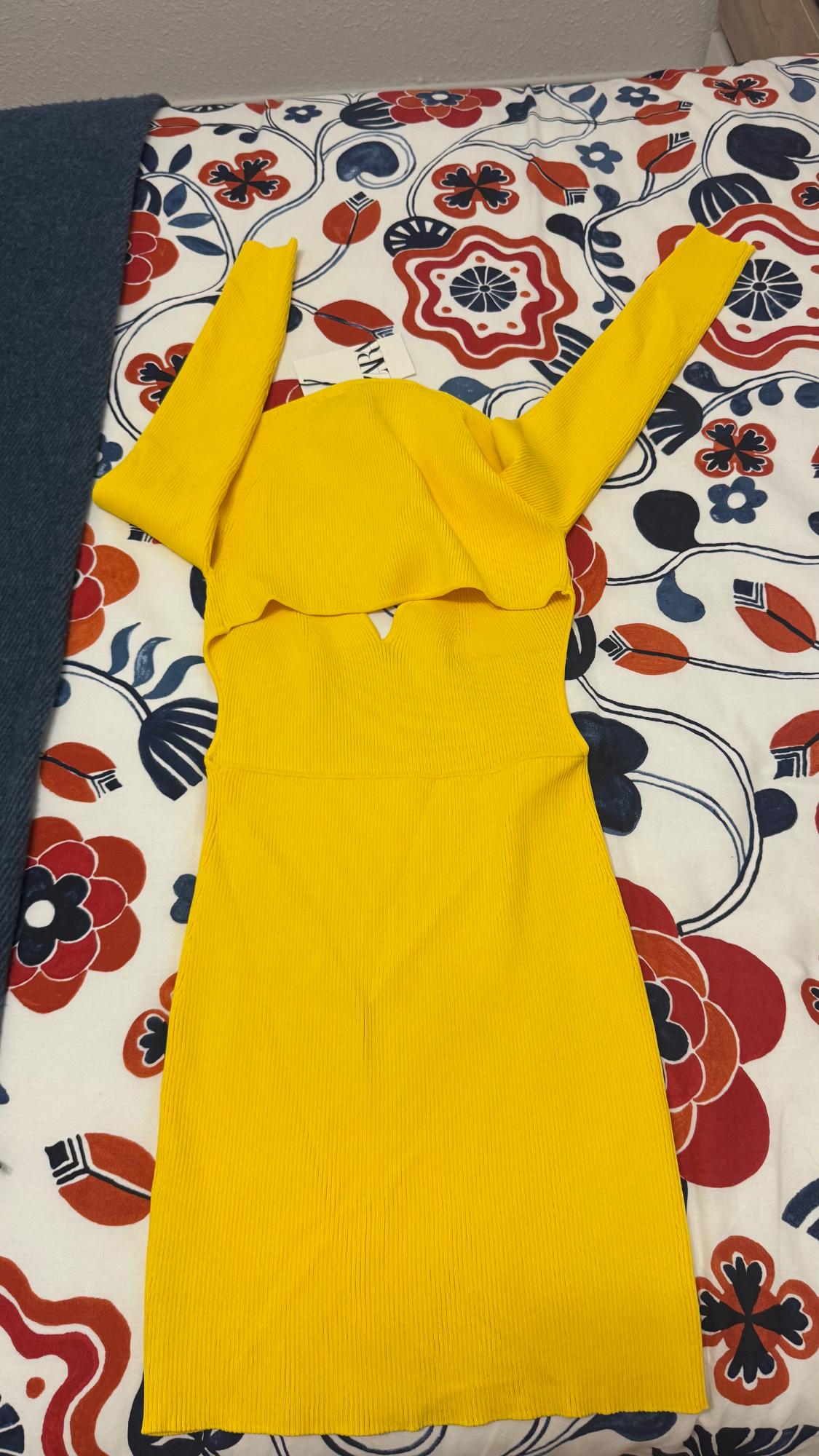 Yellow long-sleeved dress on a bed with a red and blue floral bedspread. Label visible on the dress.