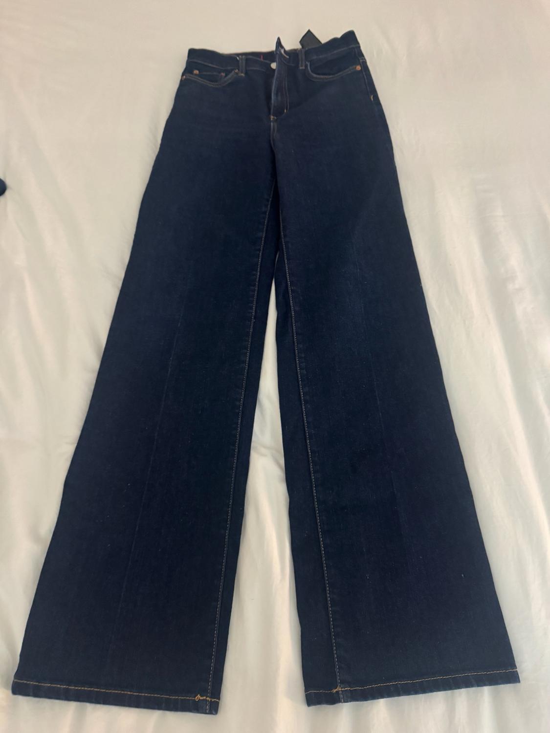 Dark blue wide-leg jeans with a front crease, on a white fabric surface.