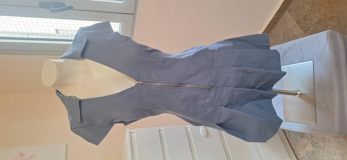 Light blue short-sleeved dress, V-neck with zip and pleated skirt on a mannequin in a room with natural light.