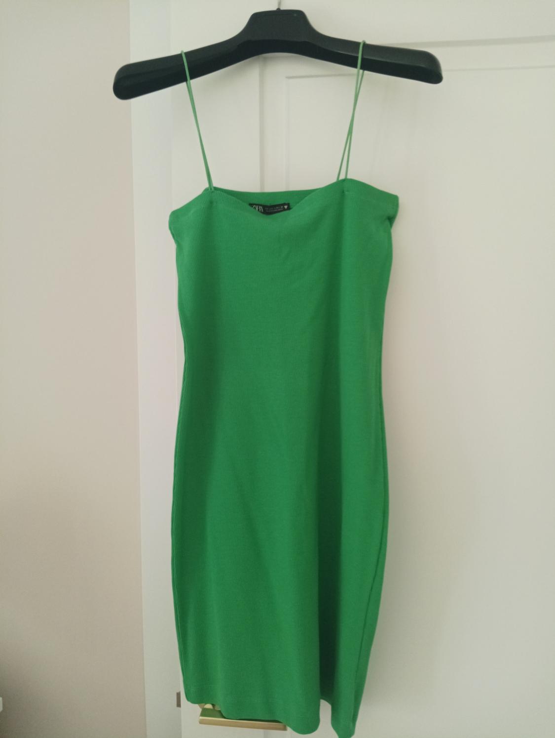 Green, thin-strapped dress hanging on a black hanger over a white door.