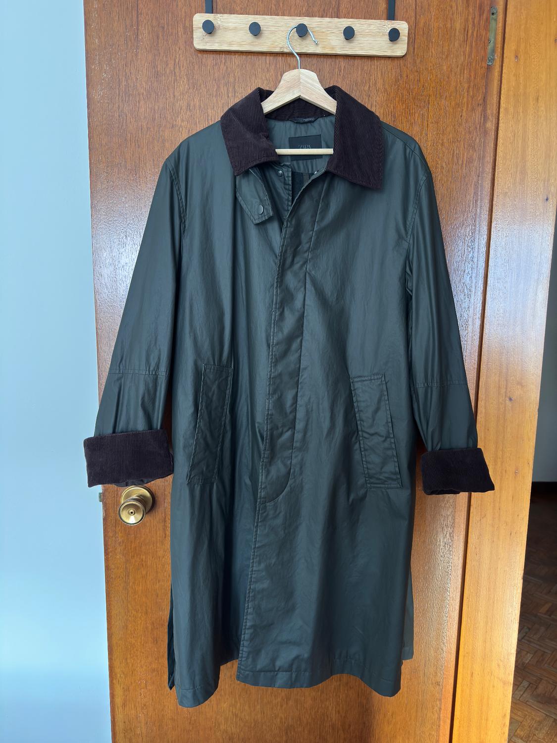 Dark green coat with a brown corduroy collar and cuffs, hanging on a wooden hanger over a wooden door.