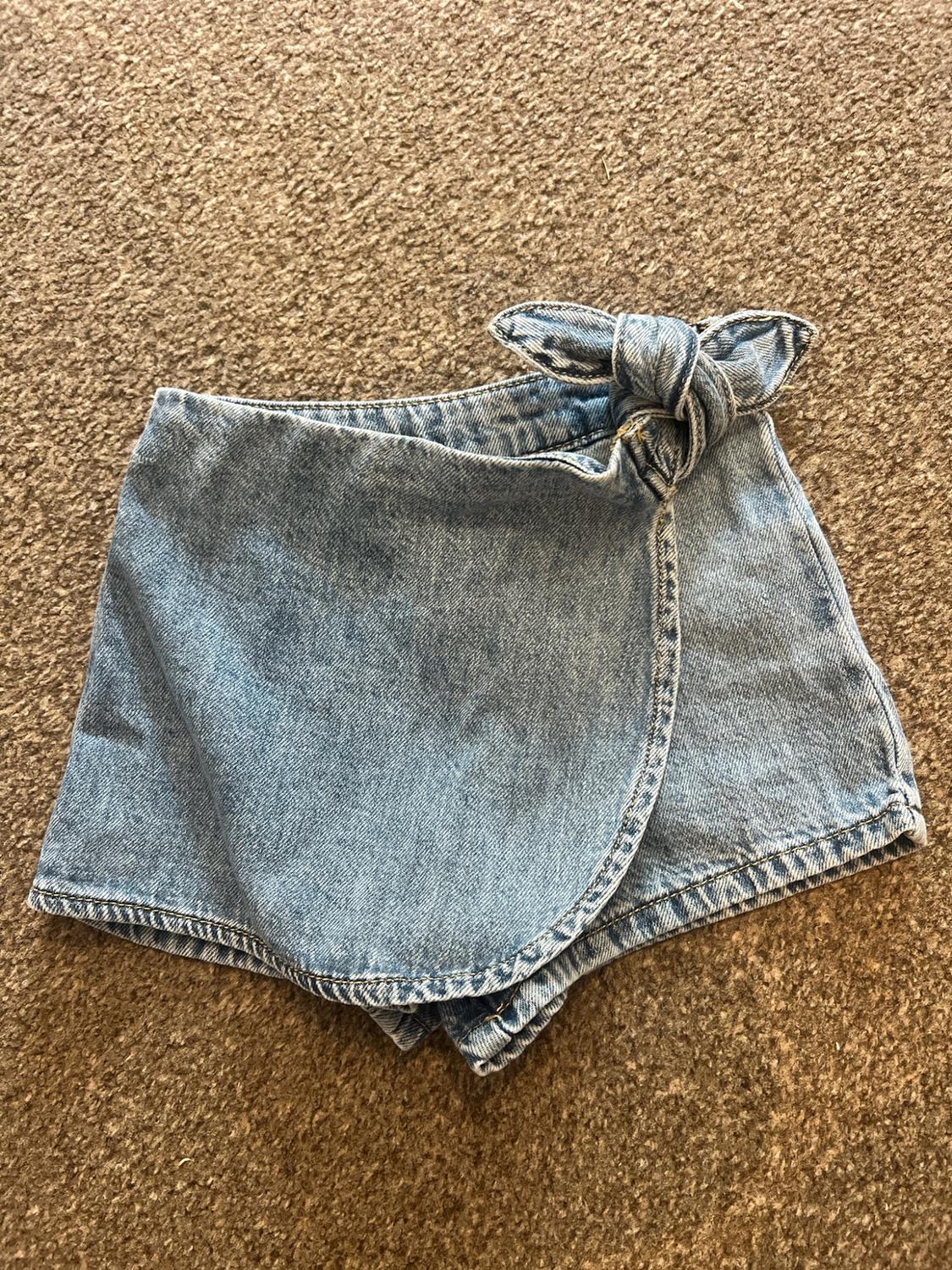 Light blue denim skort with a wrap-over panel and side tie, on a brown rug.