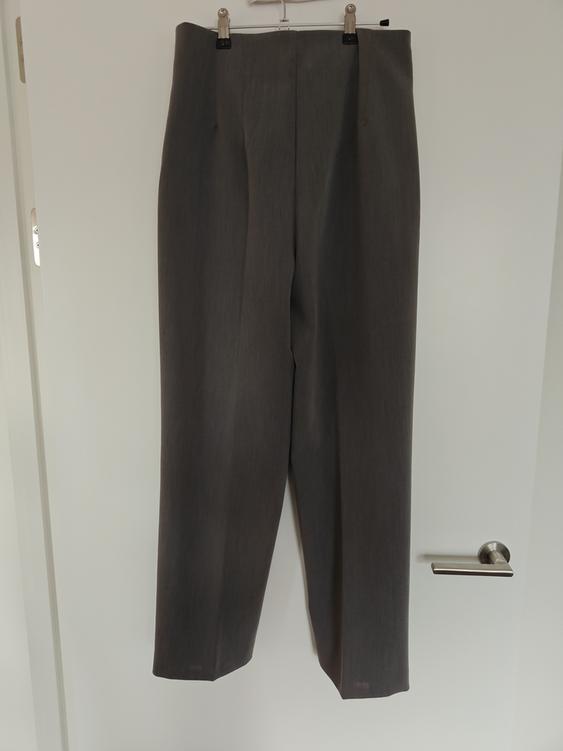 Grey trousers hanging on a hanger over a white door. The image shows a simple and elegant design.
