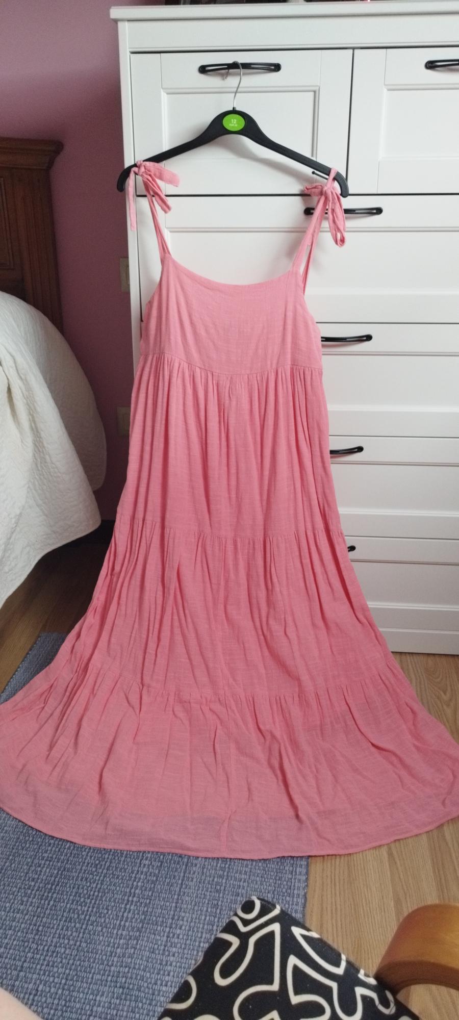 Pink maxi dress with tie straps and tiered skirt, hanging on a hanger from white furniture in a bedroom.