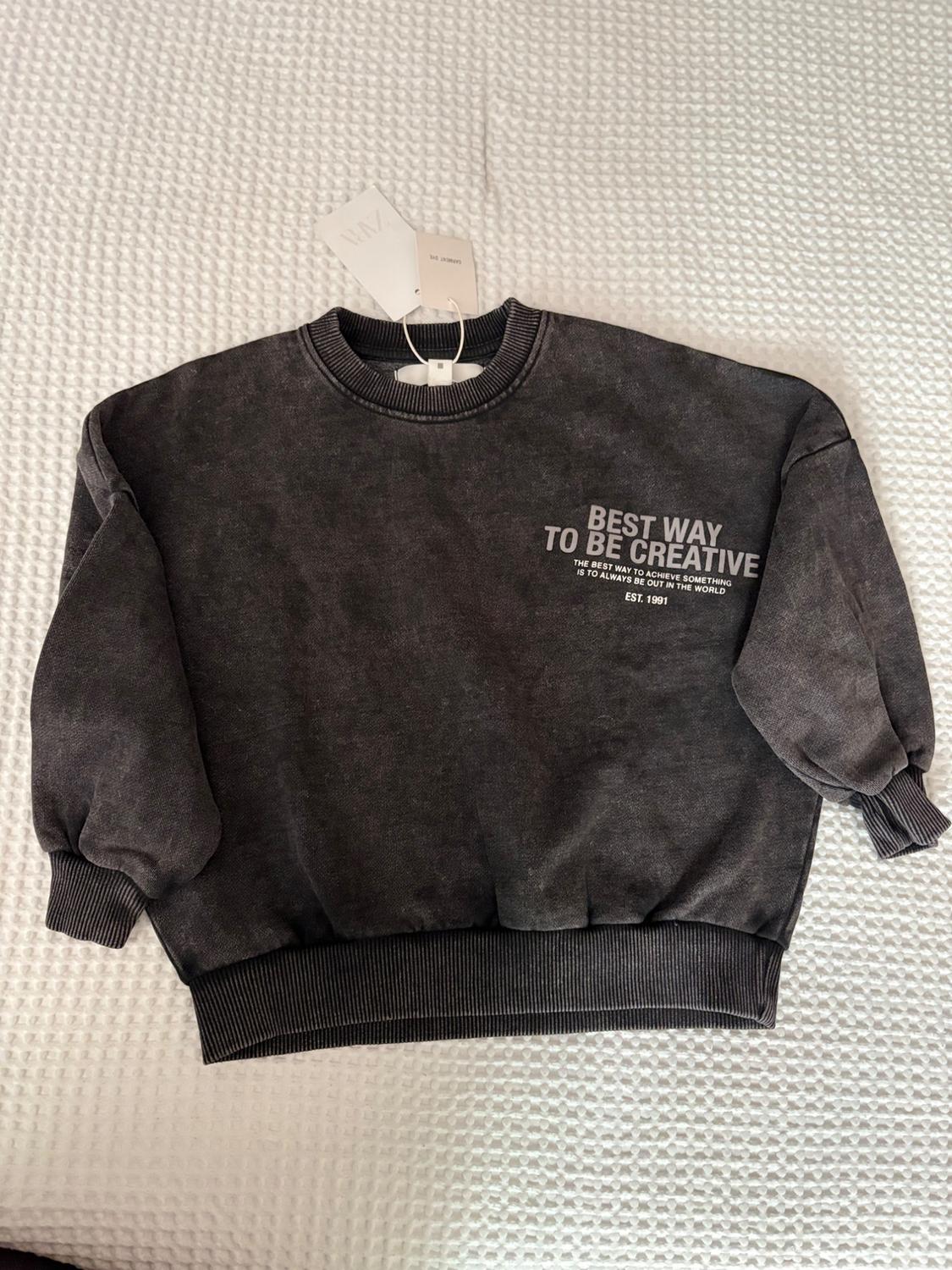 Dark gray crewneck sweatshirt with printed text on the chest: "BEST WAY TO BE CREATIVE" and a hanging price tag on a white background.