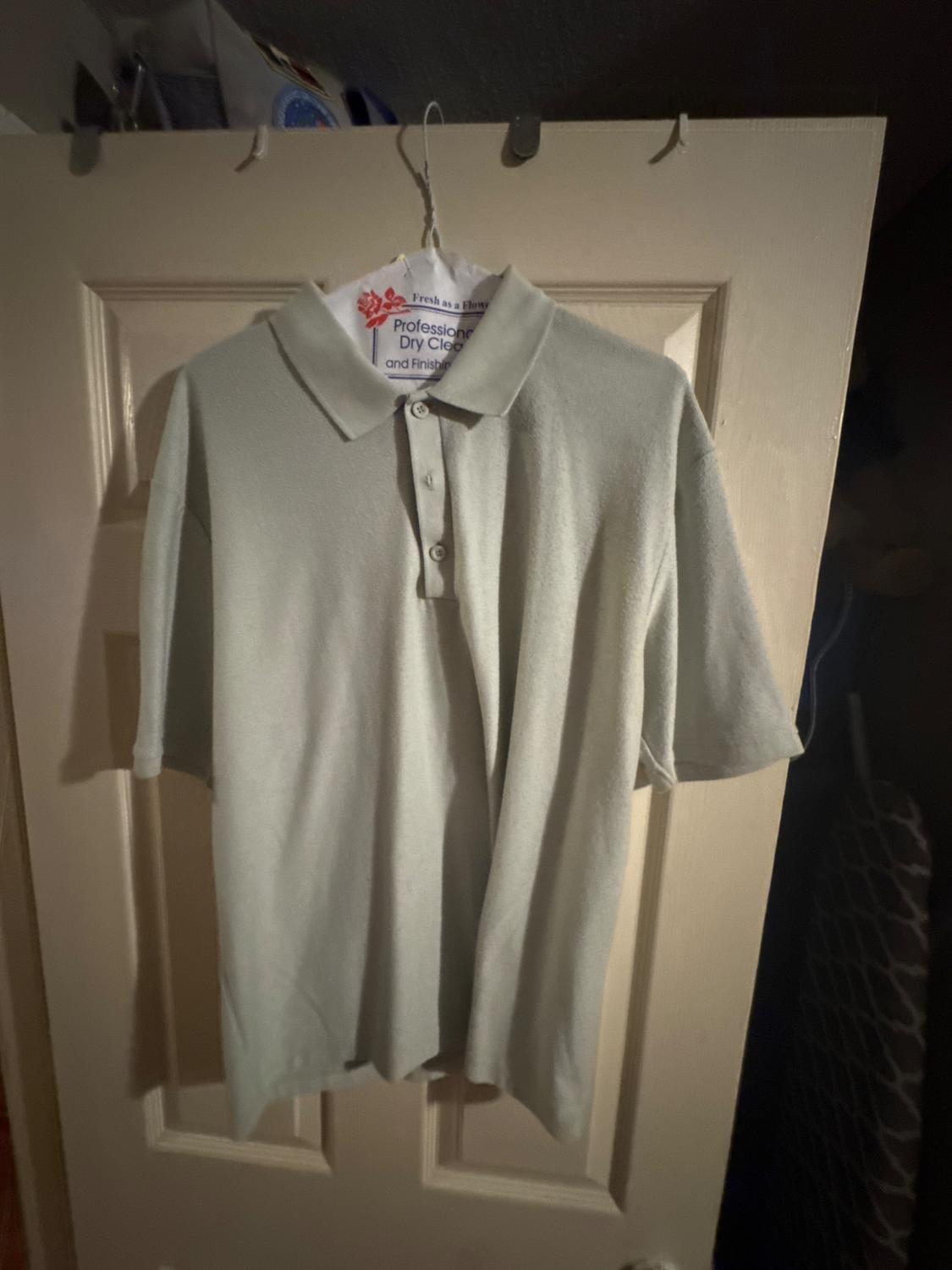 Light grey polo shirt hanging on a hanger over a door. The hanger has text: "Professional Dry Clean and Finishers".