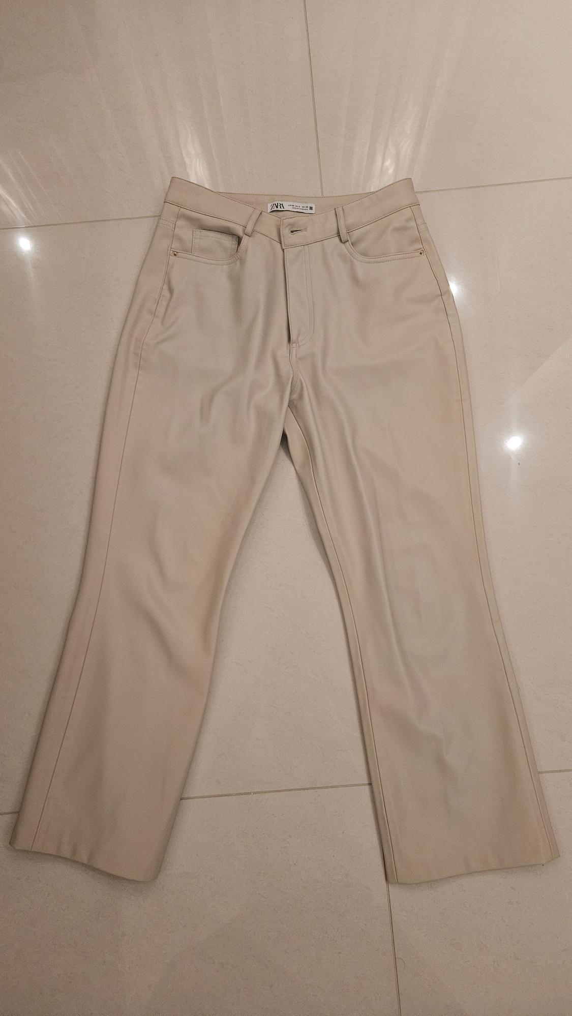 Straight-cut beige trousers on a light floor. Visible label on the waistband with the text "ZARA".