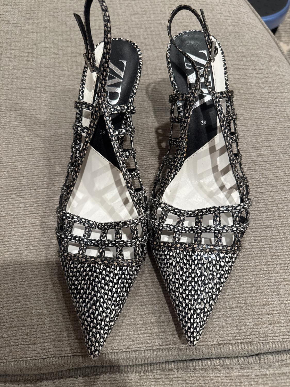 Grid-design high heels with a black and white geometric print on a grey background. Visible text: "ZARA".
