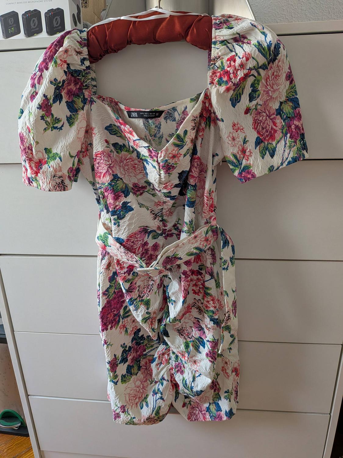 White floral print dress with puffed sleeves hanging on a chest of drawers. Text: COMPACT WIRELESS MICROPHONE SYSTEM, ZARA.