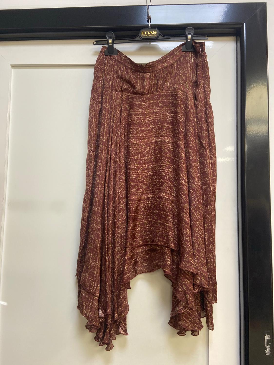 Brown skirt with a gold pattern and an asymmetric hem hanging on a white door. Text on the hanger: EDAS luxury collection.