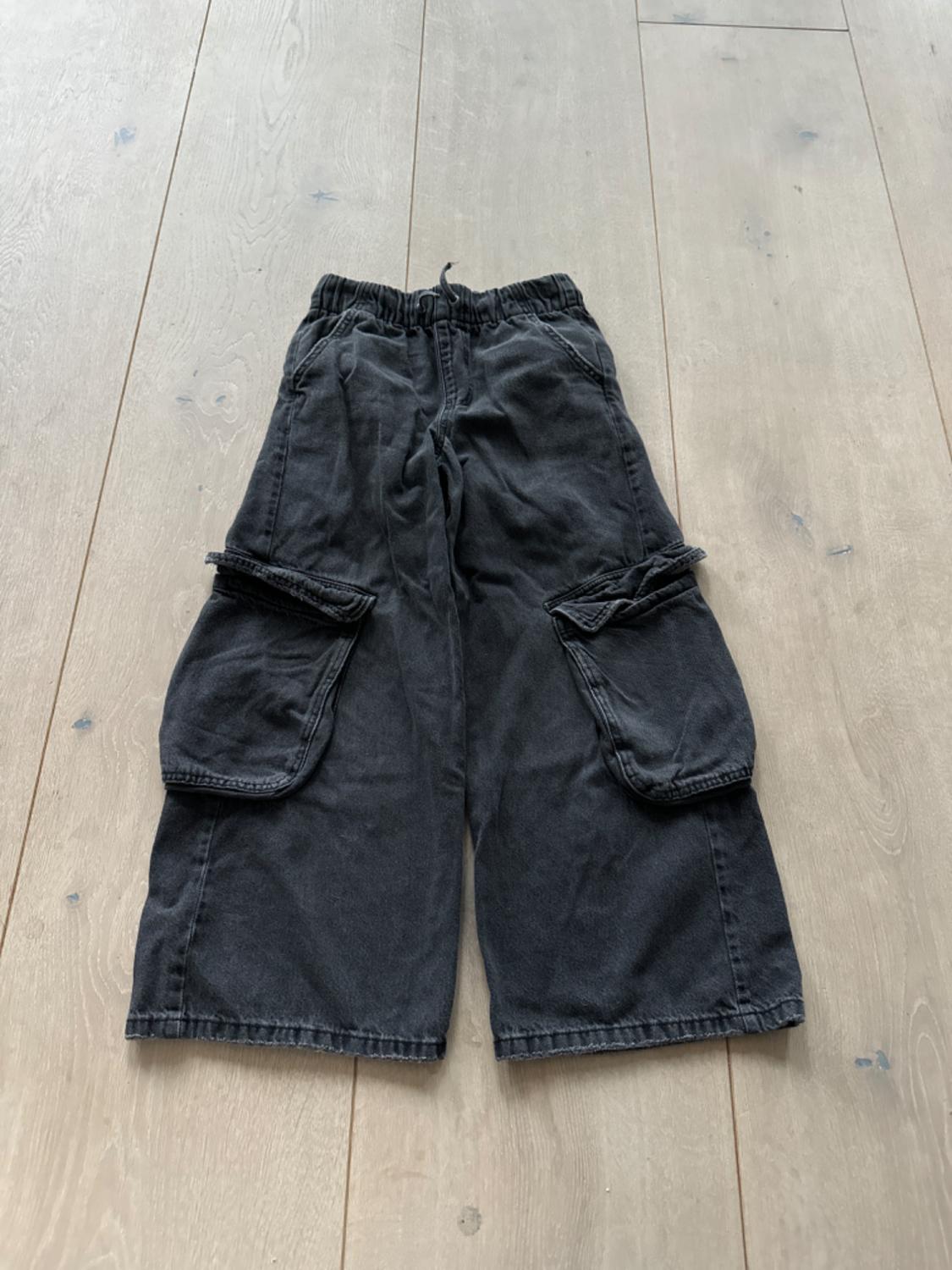 Black cargo shorts with large pockets, elasticated waist, on light wooden flooring.