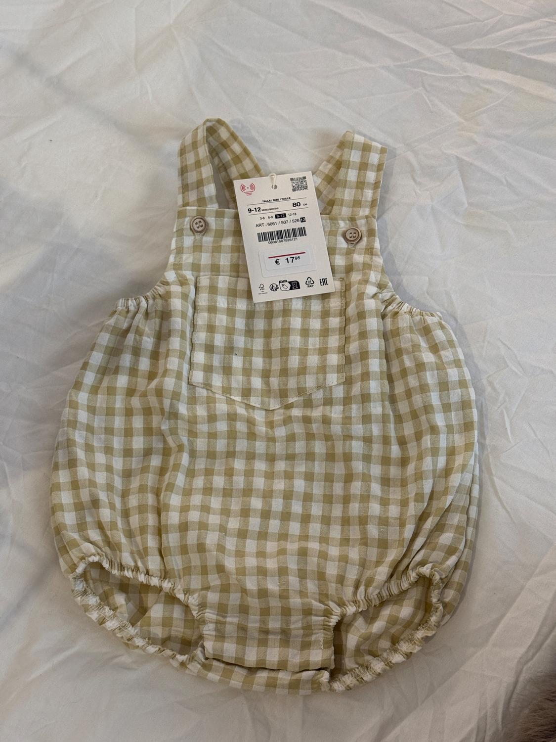 Baby's romper with beige and white checked print, buttoned straps, and a price tag of €17. Wrinkled white background.