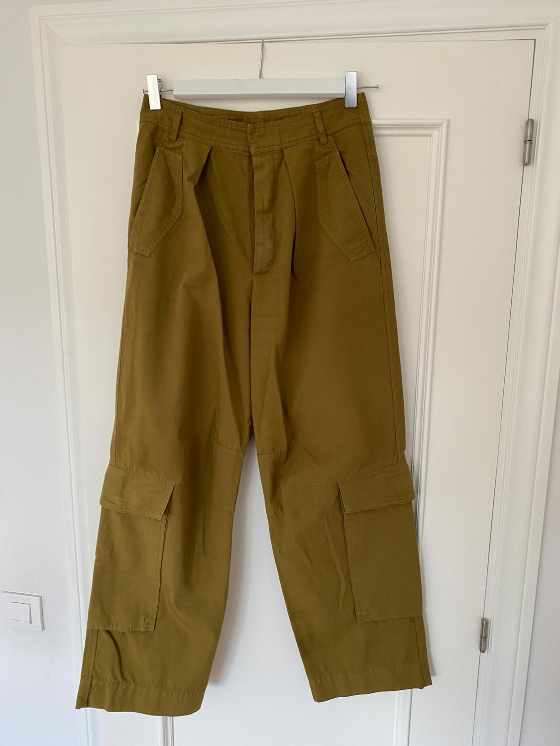 Khaki cargo trousers hung on a white hanger over a white door, with large pockets and front pleats.