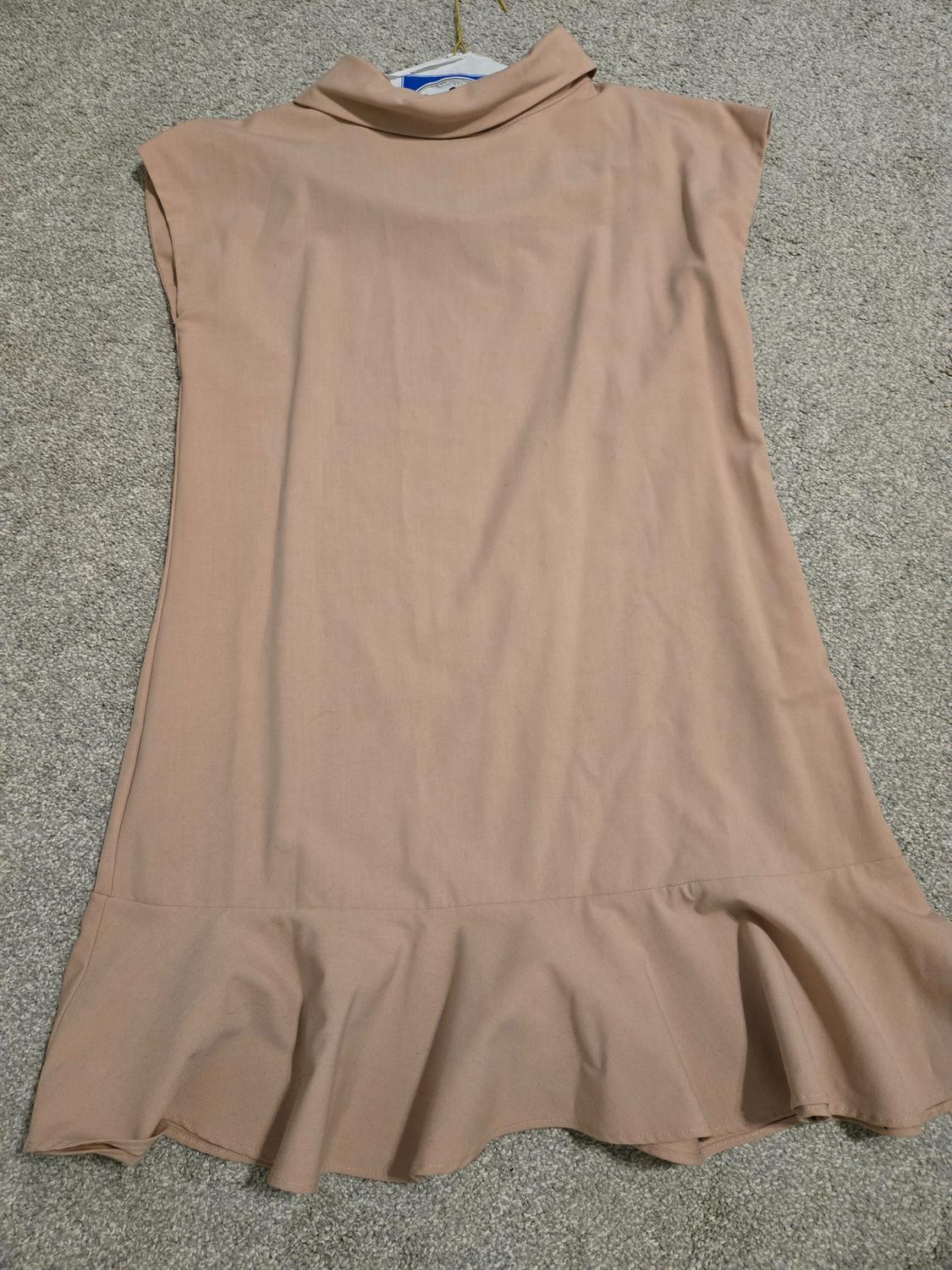Back view of a light brown dress with a high neck and a ruffle at the hem.