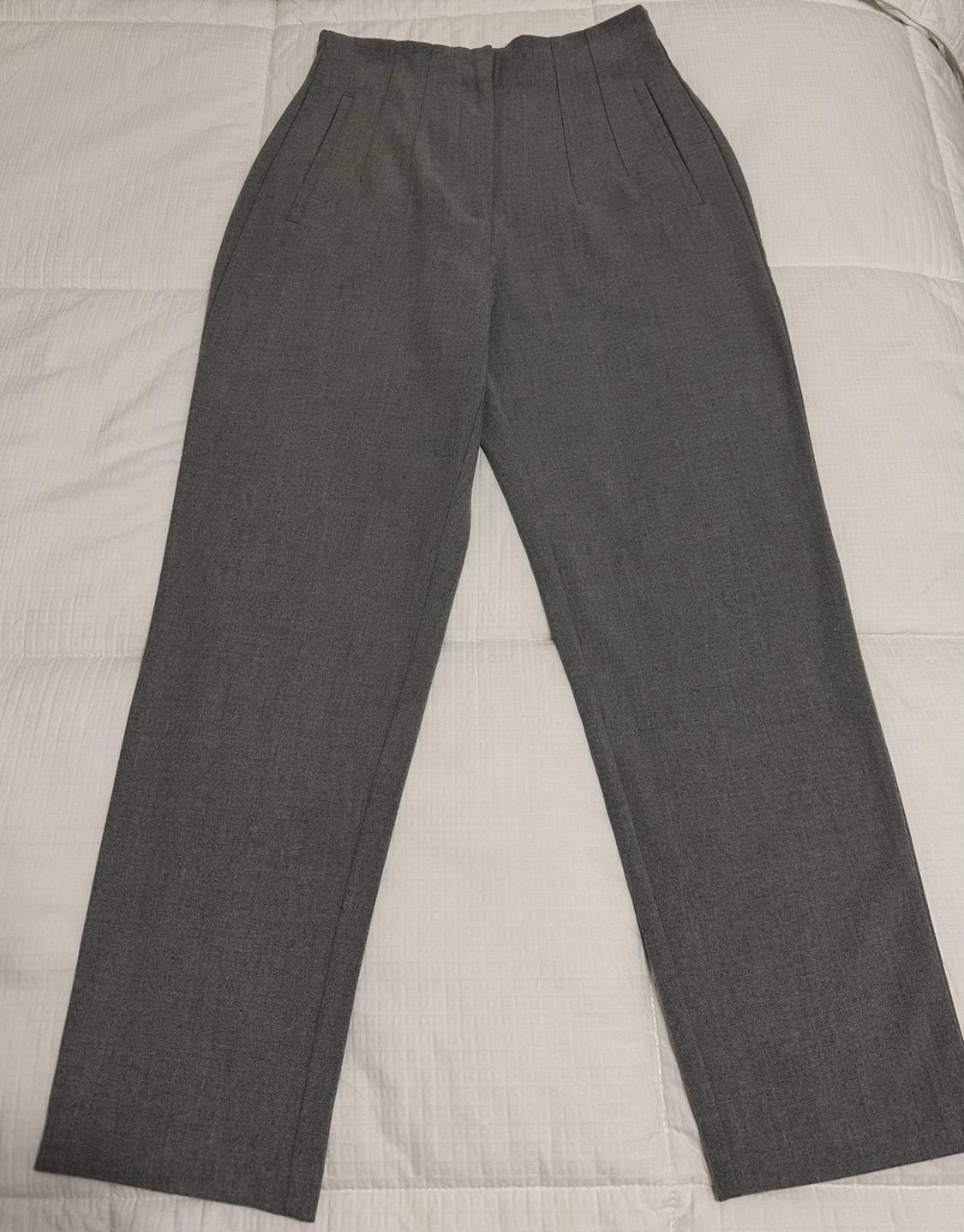 High-waisted gray pants with front pleats, laid out on a padded white surface.