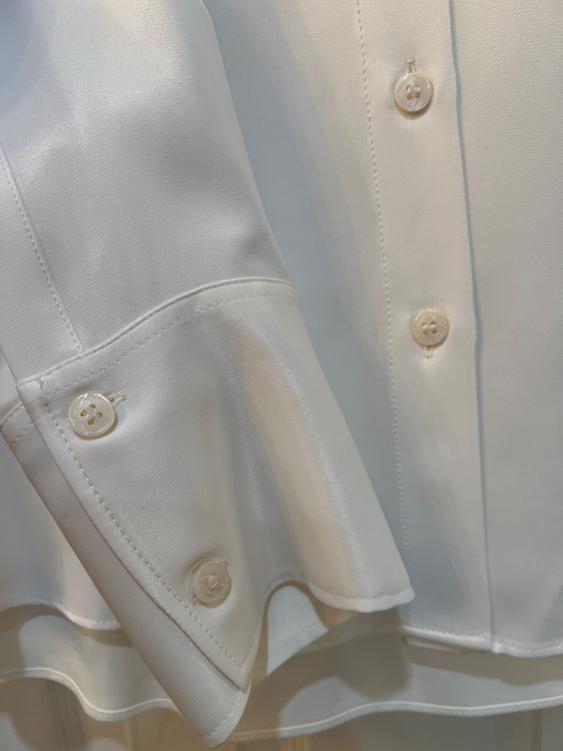 Detail of a white satin shirt with pearlescent buttons and visible seams. The fabric has a soft sheen.