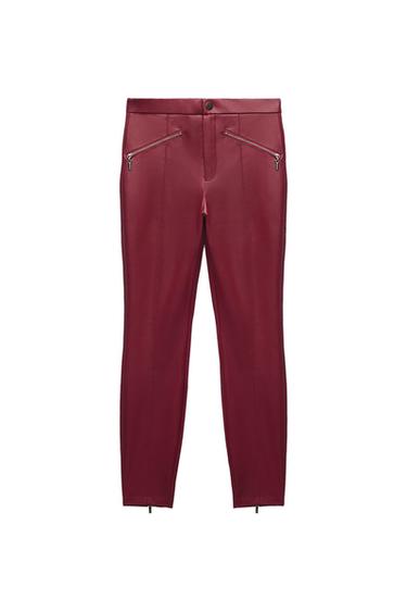 Maroon trousers with a shiny finish, featuring diagonal zip pockets, vertical seams and small zips at the hem.