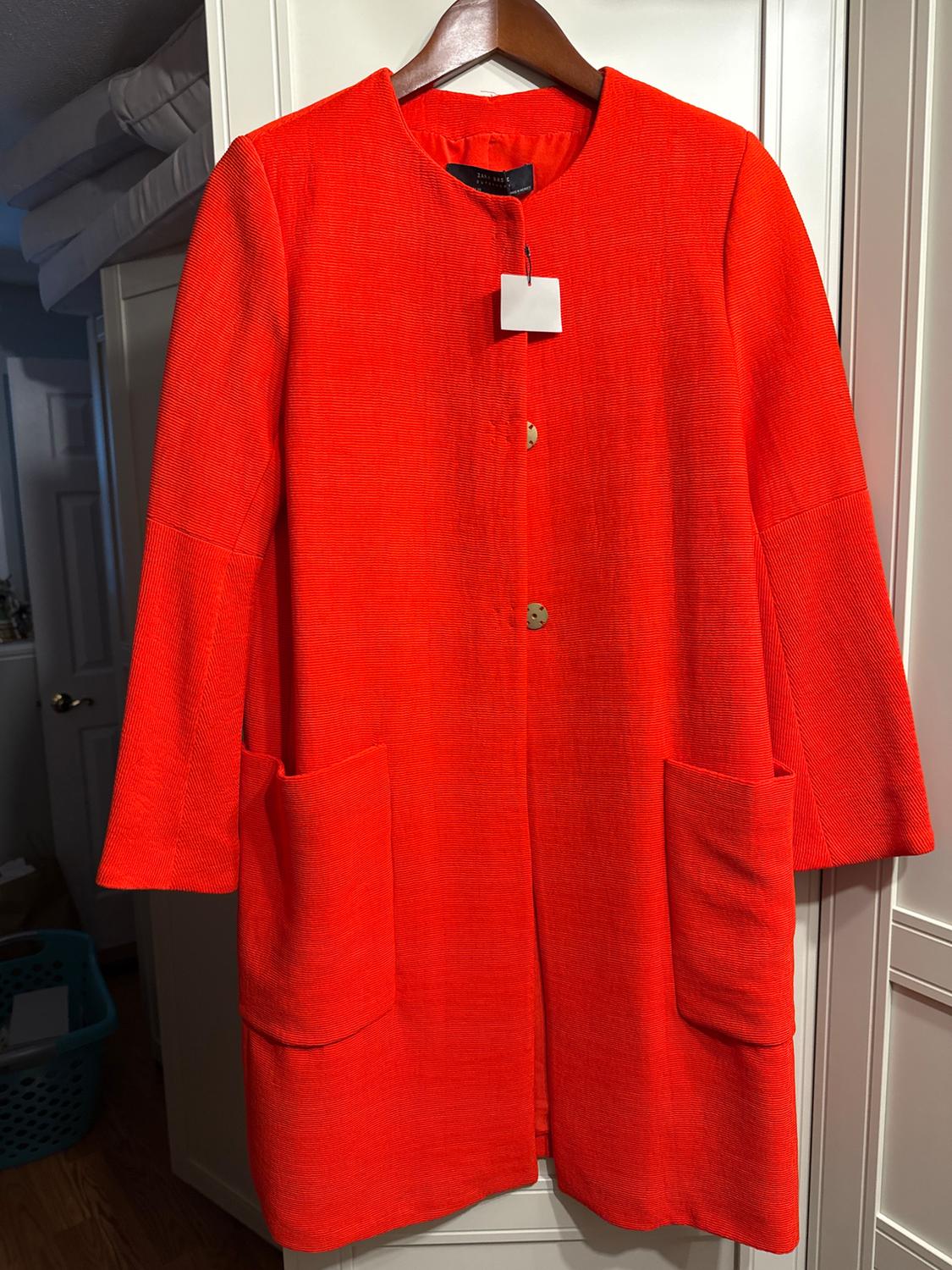 Bright red coat hanging on a wooden hanger, with large pockets and visible buttons, against a white closet background.