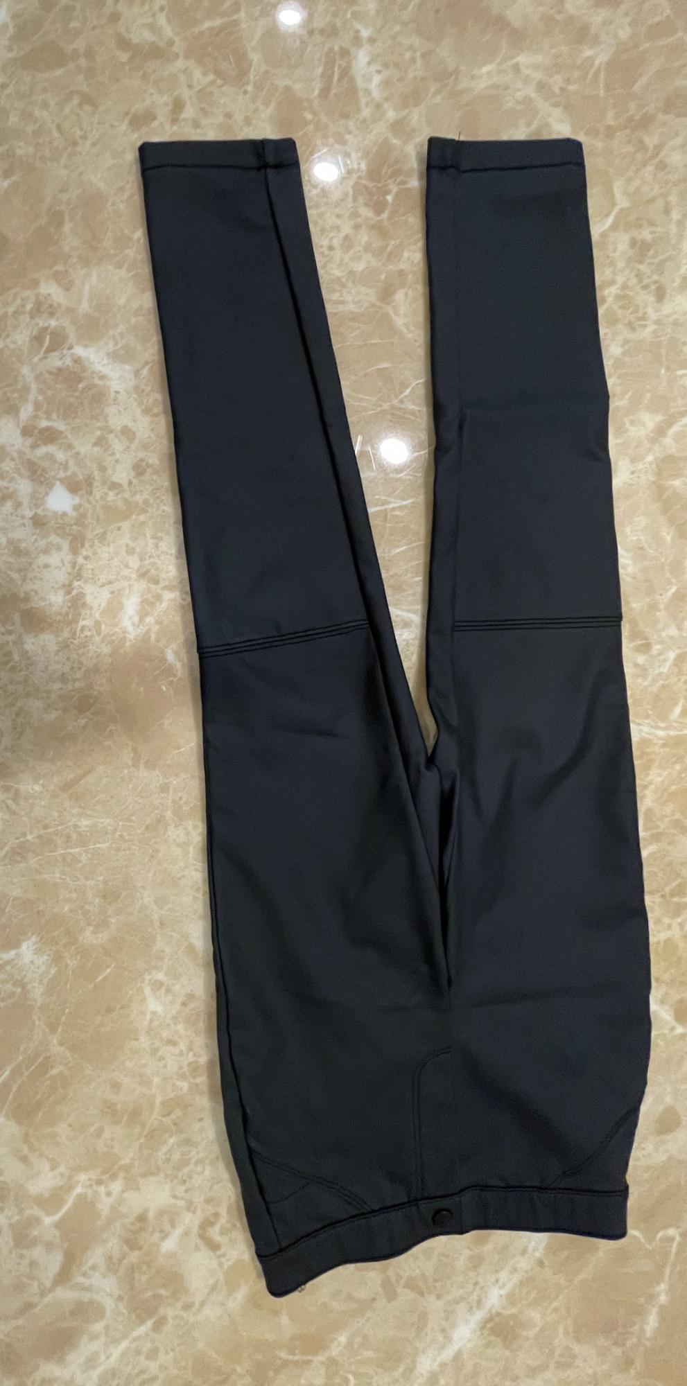 Black slim-fit trousers with knee stitching and a button fastening, laid out on a beige marble surface.