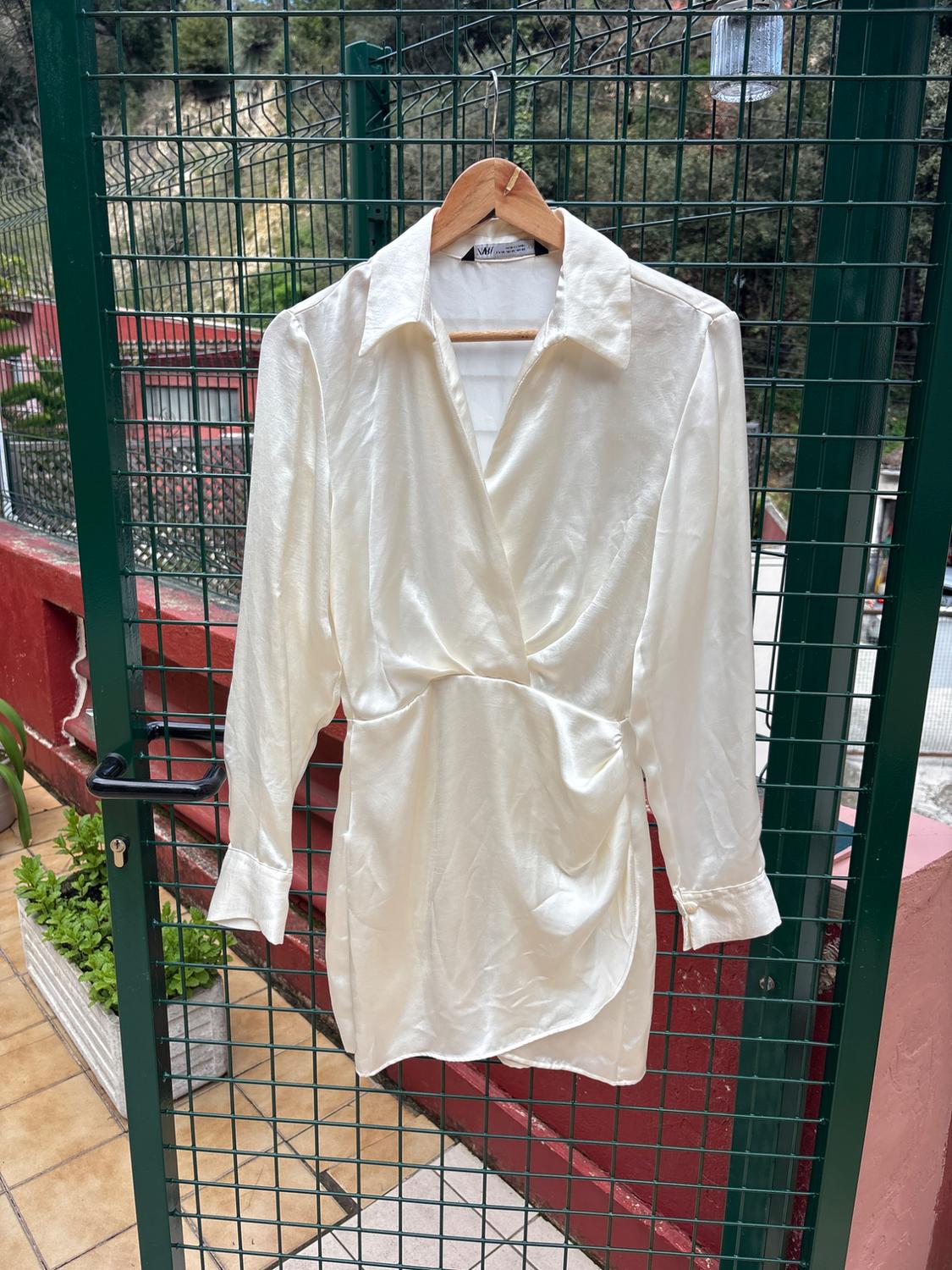 White satin dress hanging on a hanger over a metal mesh door, with a garden background and red walls.