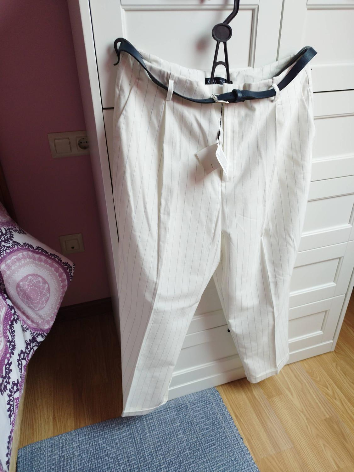 White trousers with vertical stripes hanging on a black hanger, against a white wardrobe and blue rug.