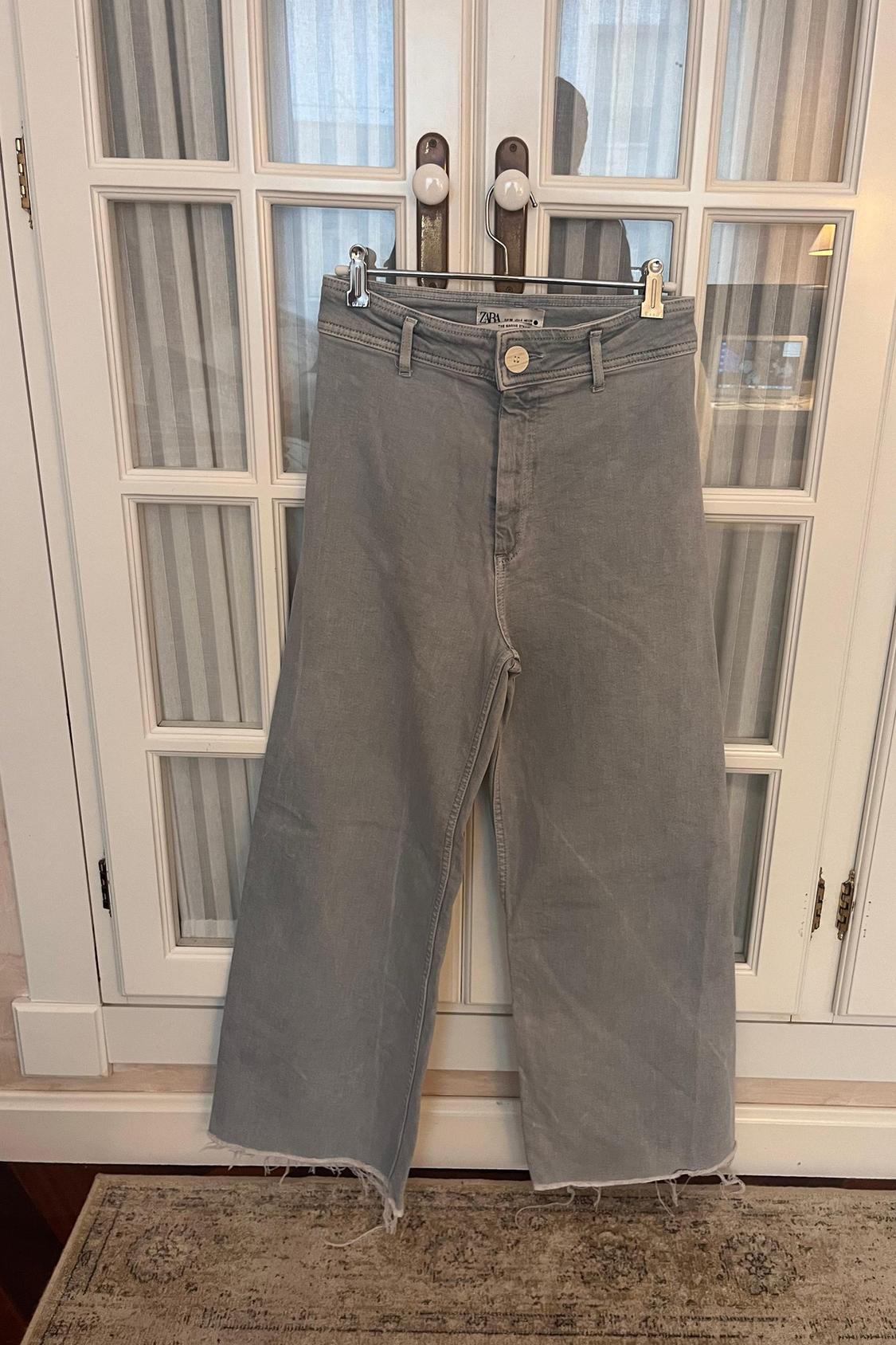 Front view of wide-leg grey trousers with frayed hem and waistband with belt loops.