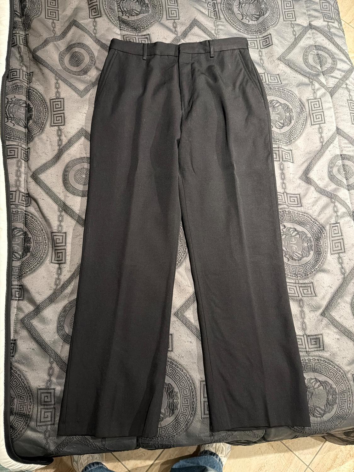 Black dress trousers on a bedspread with a geometric design in grey tones. Bottom part of shoes visible.
