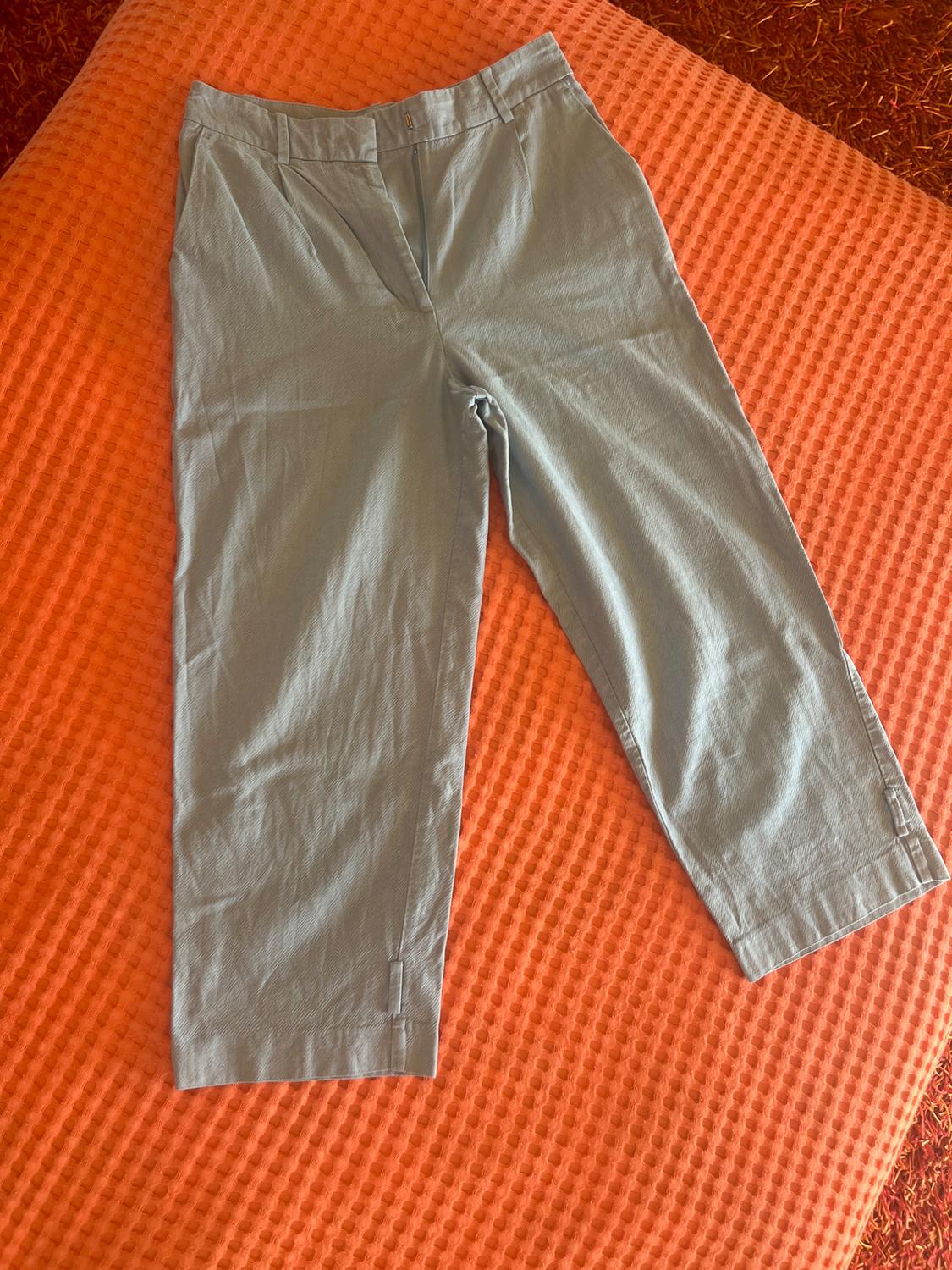 Light blue trousers with pleats and slits at the hem, laid flat on a textured orange surface. Casual style.