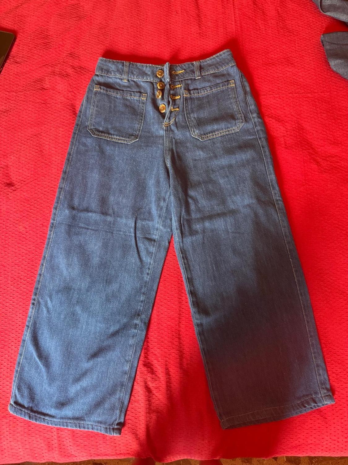 Blue high-waisted, wide-leg jeans with front buttons and patch pockets, laid flat on a red background.