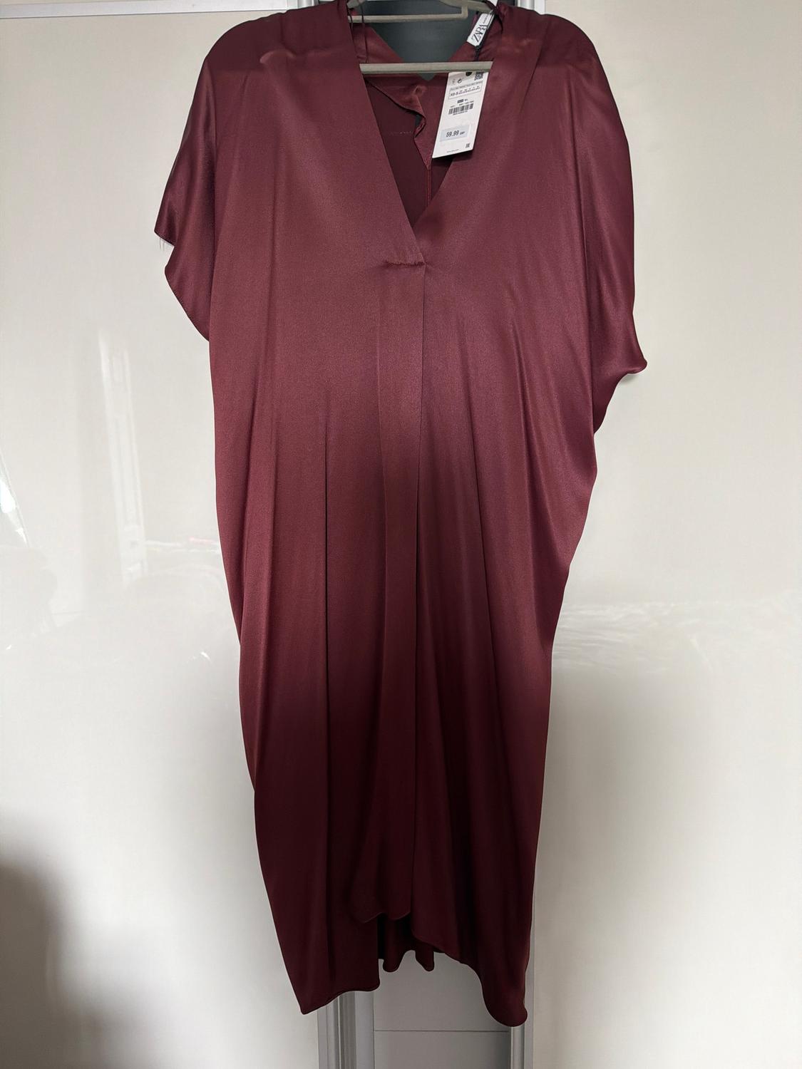 Burgundy satin dress hanging on a hanger, with a visible tag, against a white background.