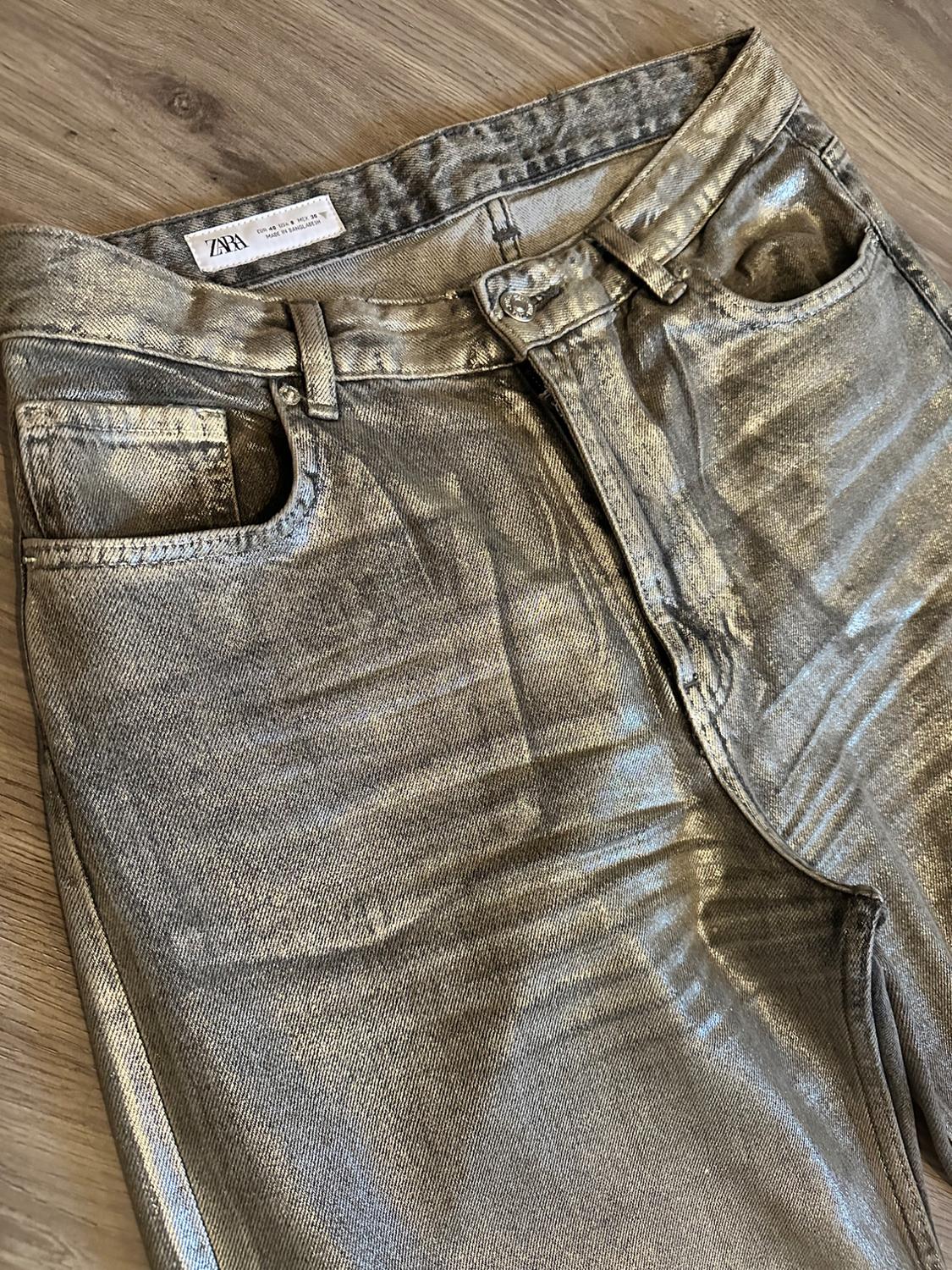 Silver metallic jeans on a wooden floor, with a visible Zara label on the waist.