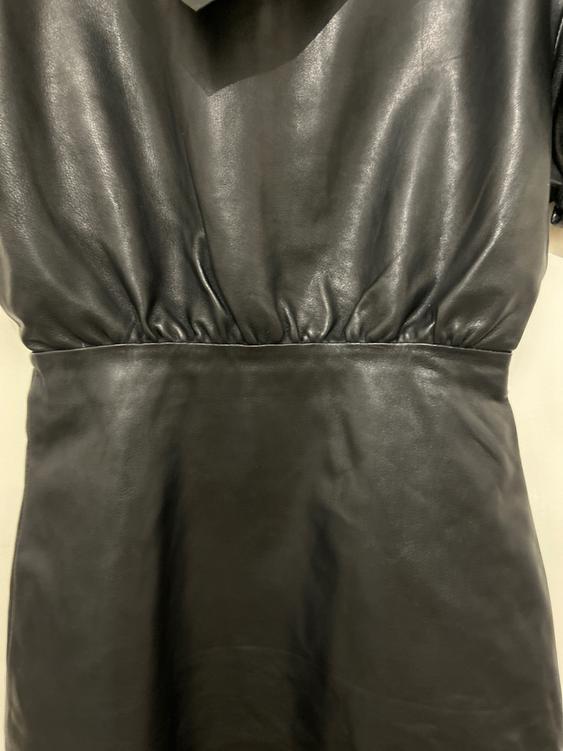 Black dress made of shiny material with ruching at the waist, close-up. The texture softly reflects the light.