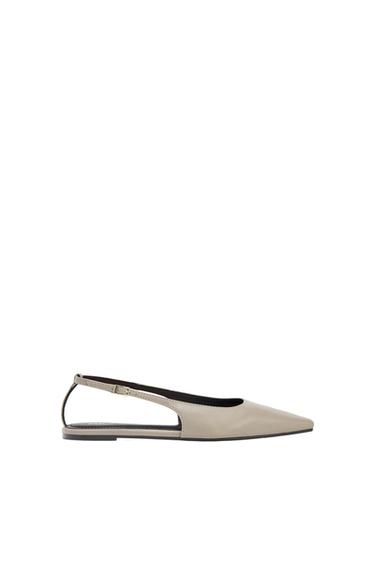 Beige flat shoe with a pointed toe and adjustable back strap, on a white background.