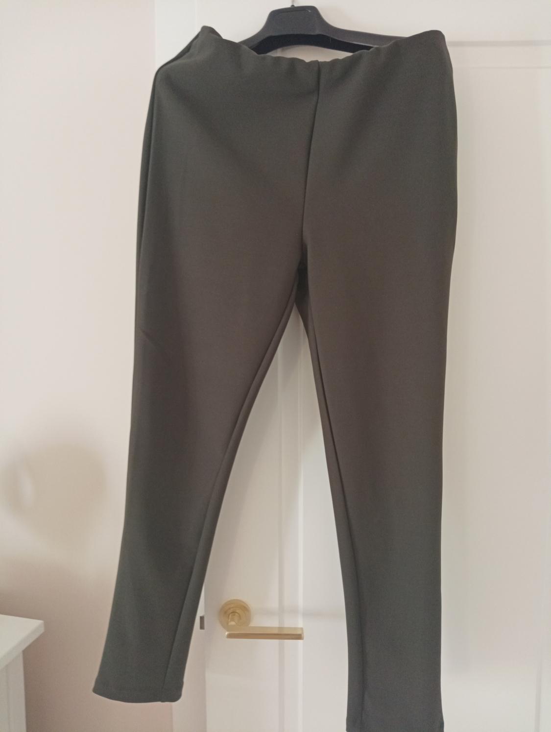 Grey trousers hanging on a black hanger over a white door. Indoor setting with soft lighting.