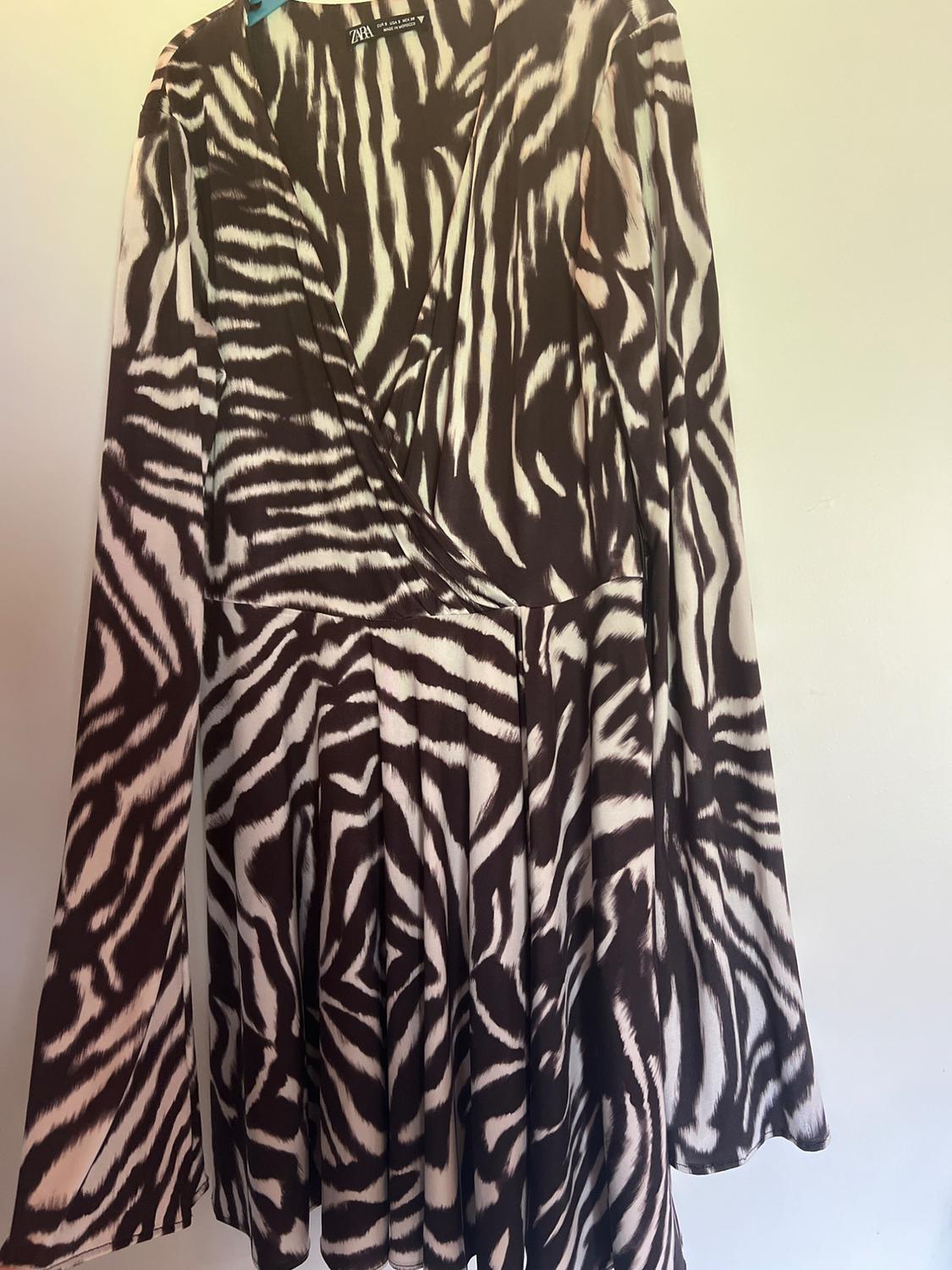 Short, long-sleeved wrap dress with a zebra print, hanging on a hanger against a white background. Label with the text ZARA.