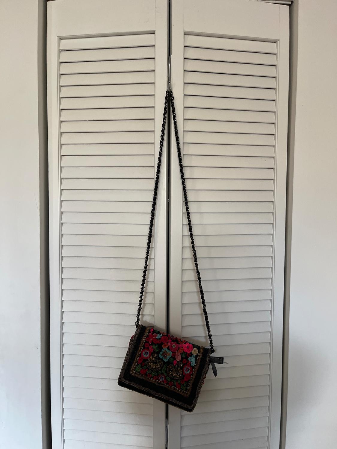 Handbag hanging on a white panelled door. Colourful floral design and black chain. Simple and minimalist background.