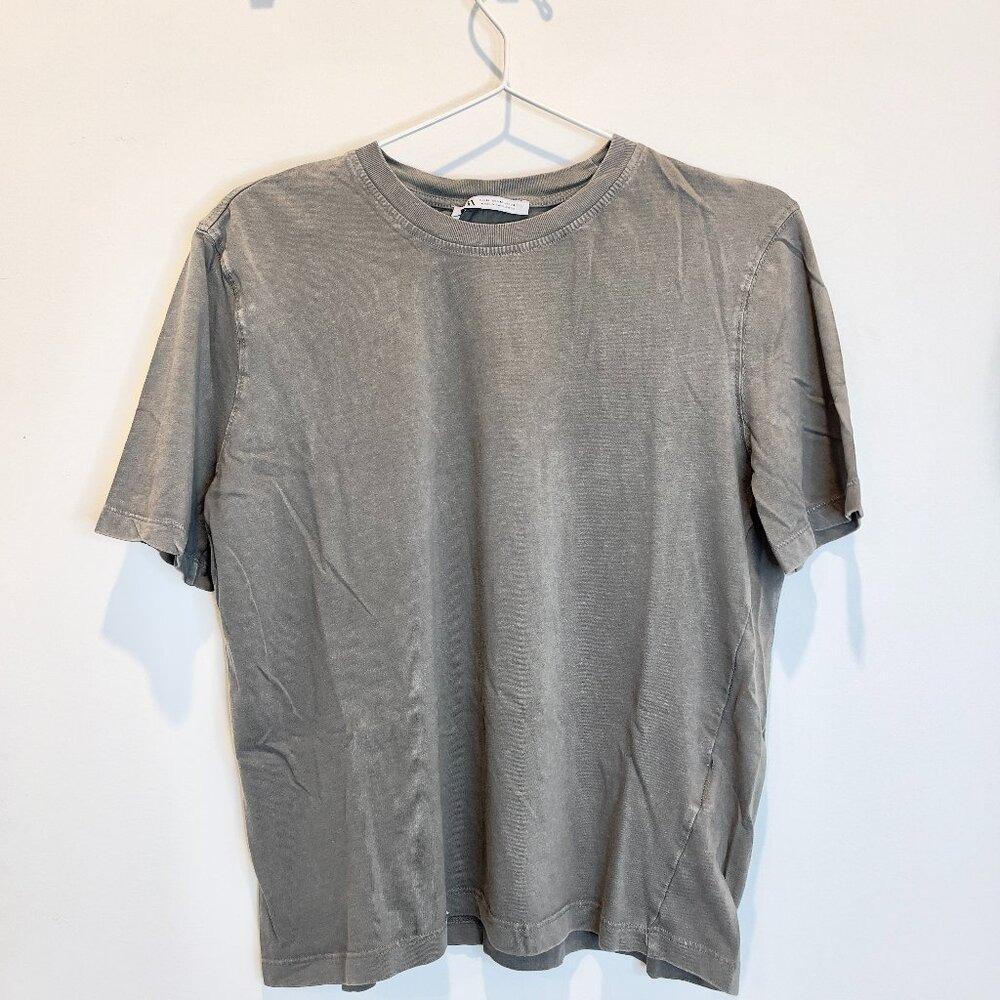Gray short-sleeve T-shirt with a washed finish, a crew neck, and a Zara label, hanging on a hanger on a white wall.