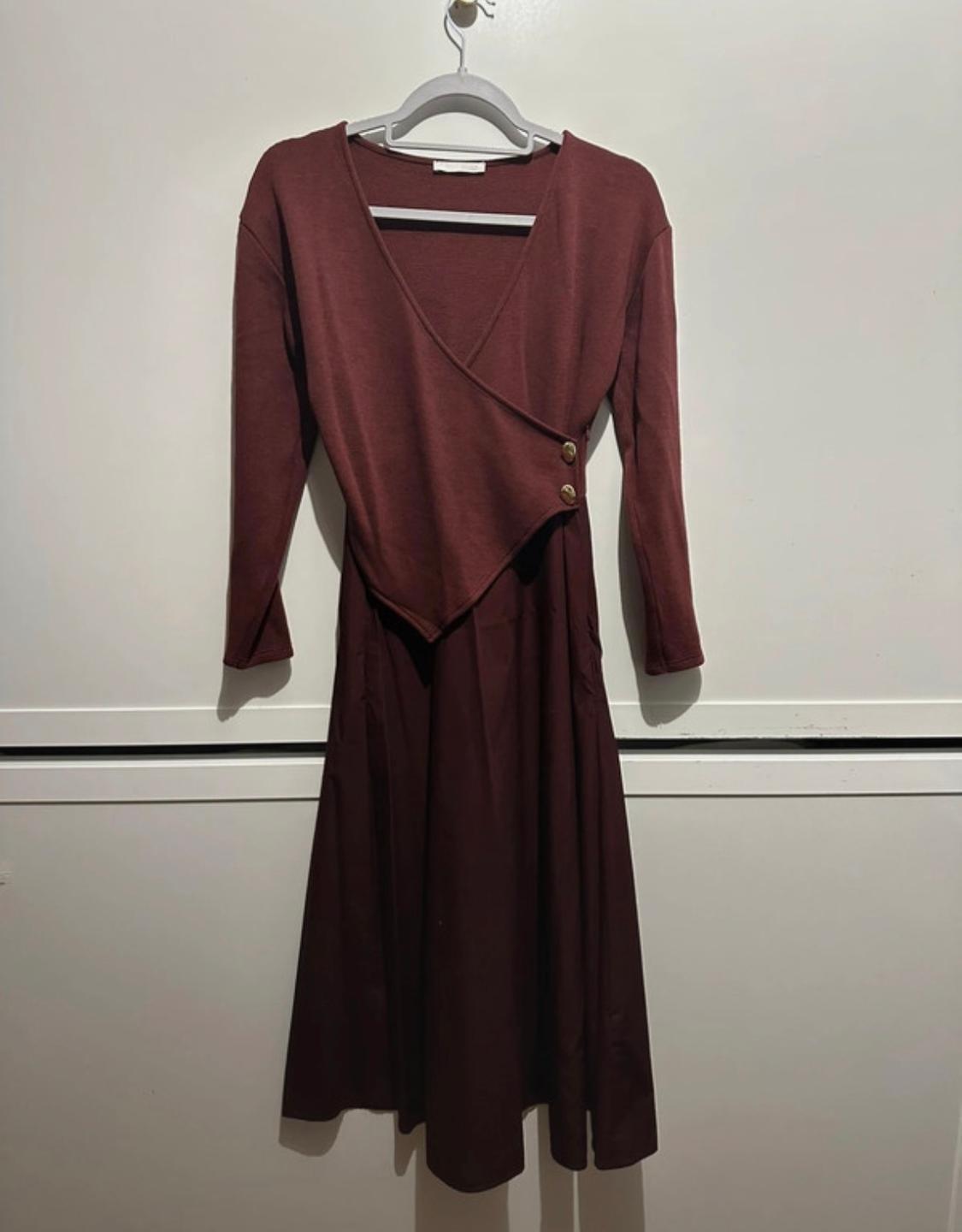 Long-sleeved brown dress with a crossover neckline and buttons on the side, hanging on a hanger against a white background.