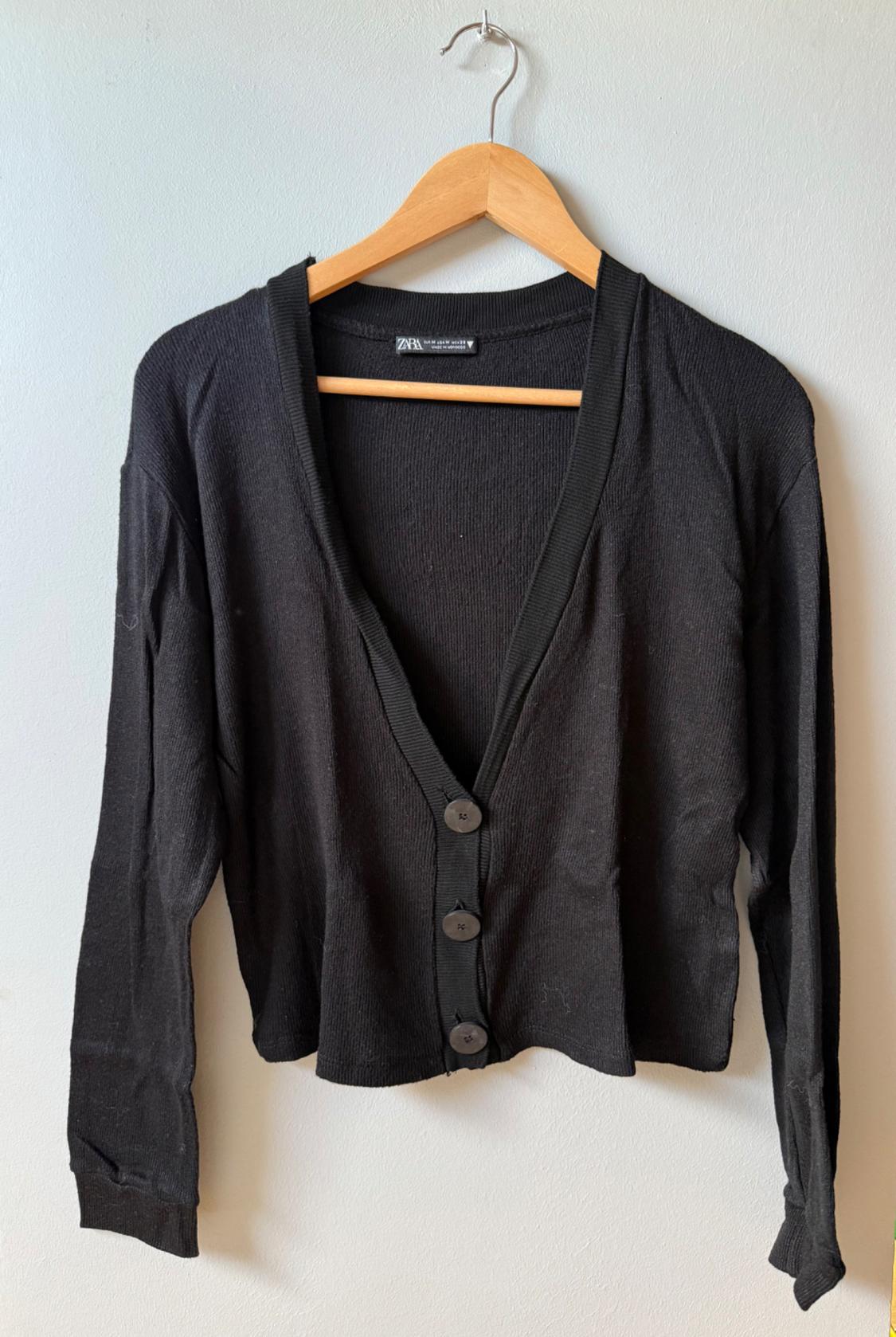 Black long-sleeved cardigan with large buttons, hanging on a wooden hanger against a white background.