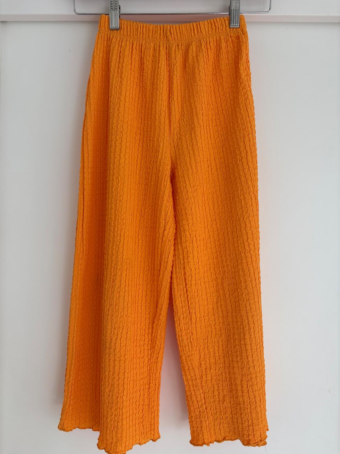 Bright orange crinkled fabric wide-leg trousers hanging on a hanger against a white background.