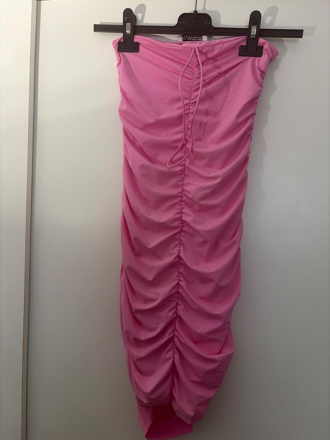 Pink strapless ruched bandeau dress hanging on a black hanger against a white background.