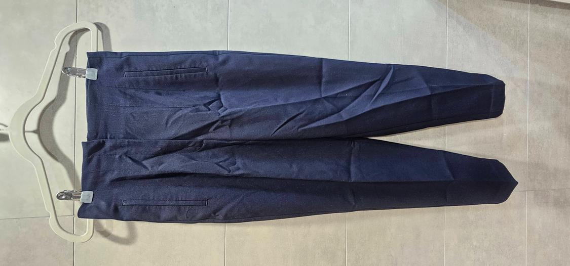 Navy blue trousers hanging on a white clothes hanger with pegs against a light-tiled floor.
