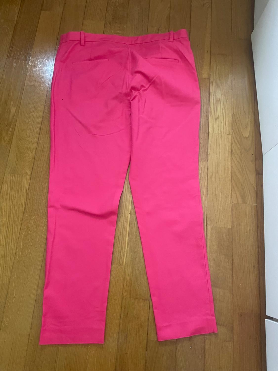 Fuchsia trousers in a plain fabric on a light wood floor, seen from behind, with back pockets and belt loops.