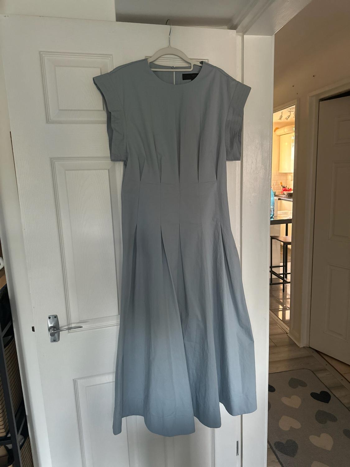Light blue short-sleeved midi dress with pleats at the waist, hanging on a white door inside a house.