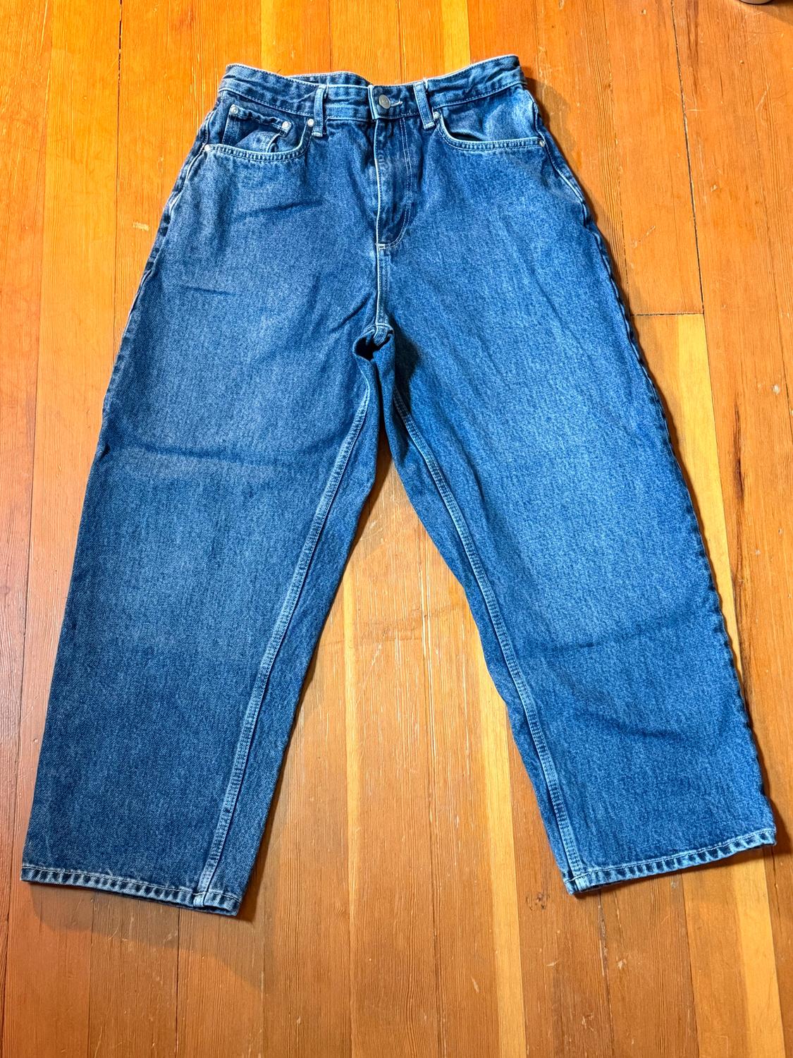 Straight-cut blue jeans on a light wooden floor. Classic five-pocket design with button fastening.