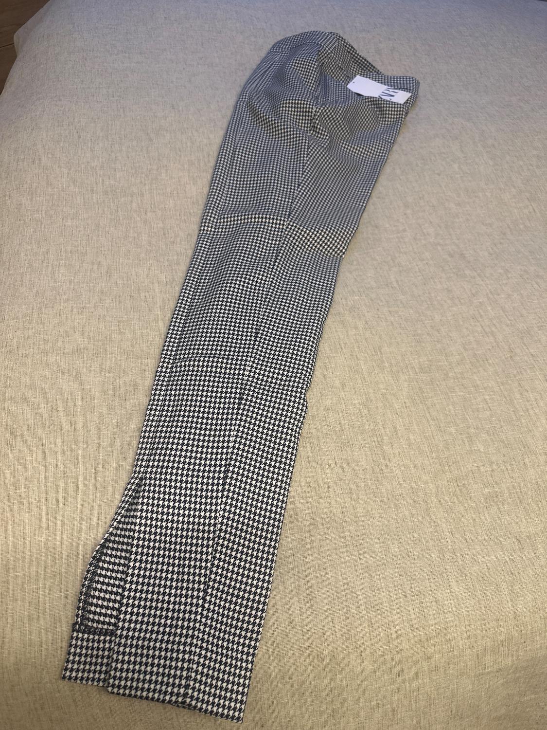 Black and white checked trousers laid out on a beige surface. White label visible at the waist.